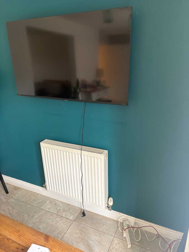 Wall-mounted TV with visible power cable before additional socket installation